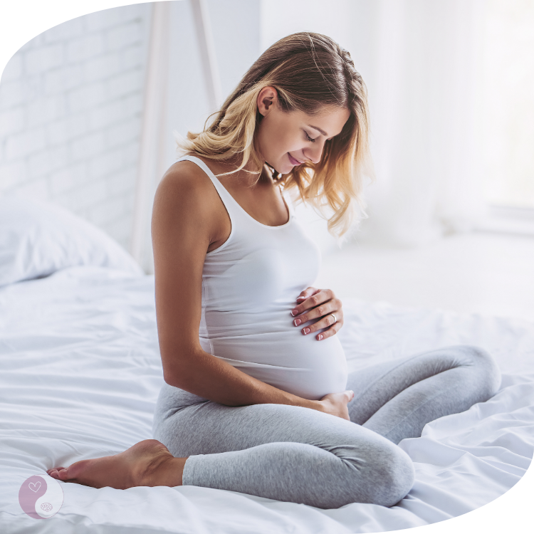 frau-schwanger-bett-happy Glückliche schwangere Frau sitzt auf einem Bett und hält ihren Babybauch